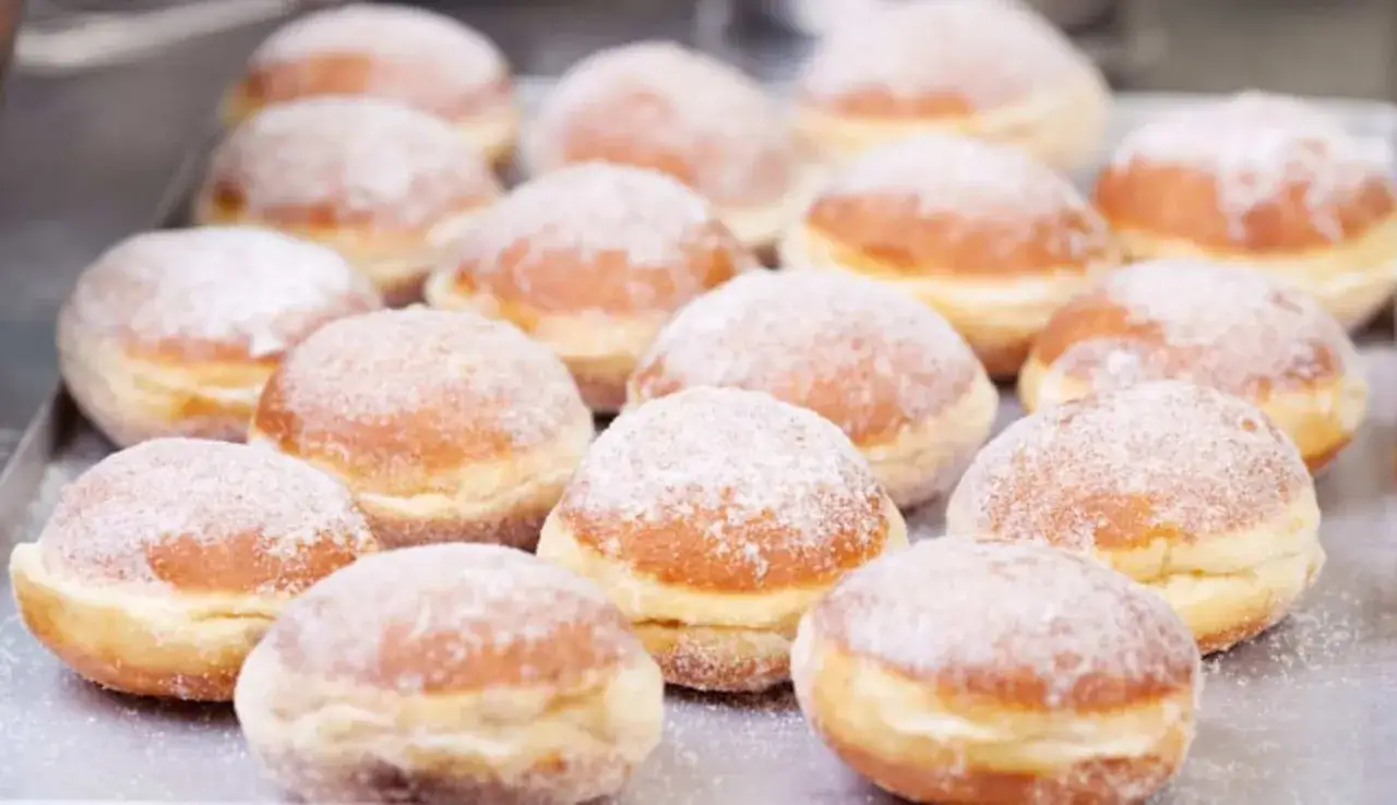 Una fila di bomboloni ricetta originale, dorati e cosparsi di zucchero a velo, pronti per essere gustati.