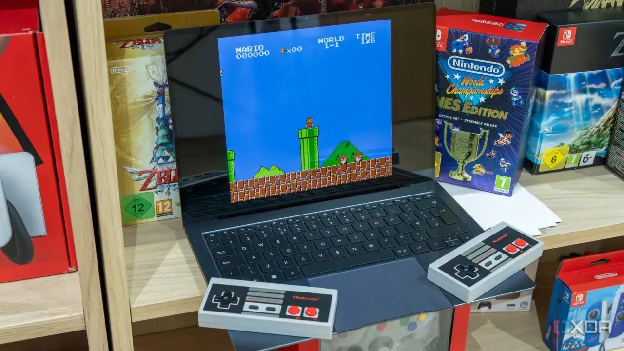 Laptop z grą Super Mario Bros. uruchomioną przez DOSBox, obok pudełka z grami Nintendo i kontrolerów.