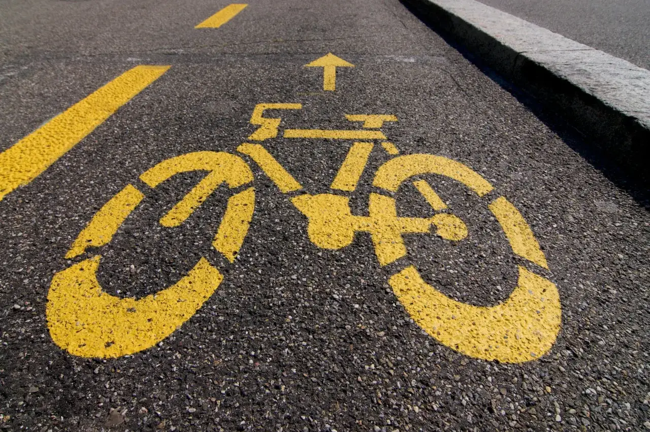 Gelber Fahrradsymbol-Aufdruck auf Asphalt, der einen pop-up Radweg markiert. Ein Pfeil zeigt die Fahrtrichtung an.