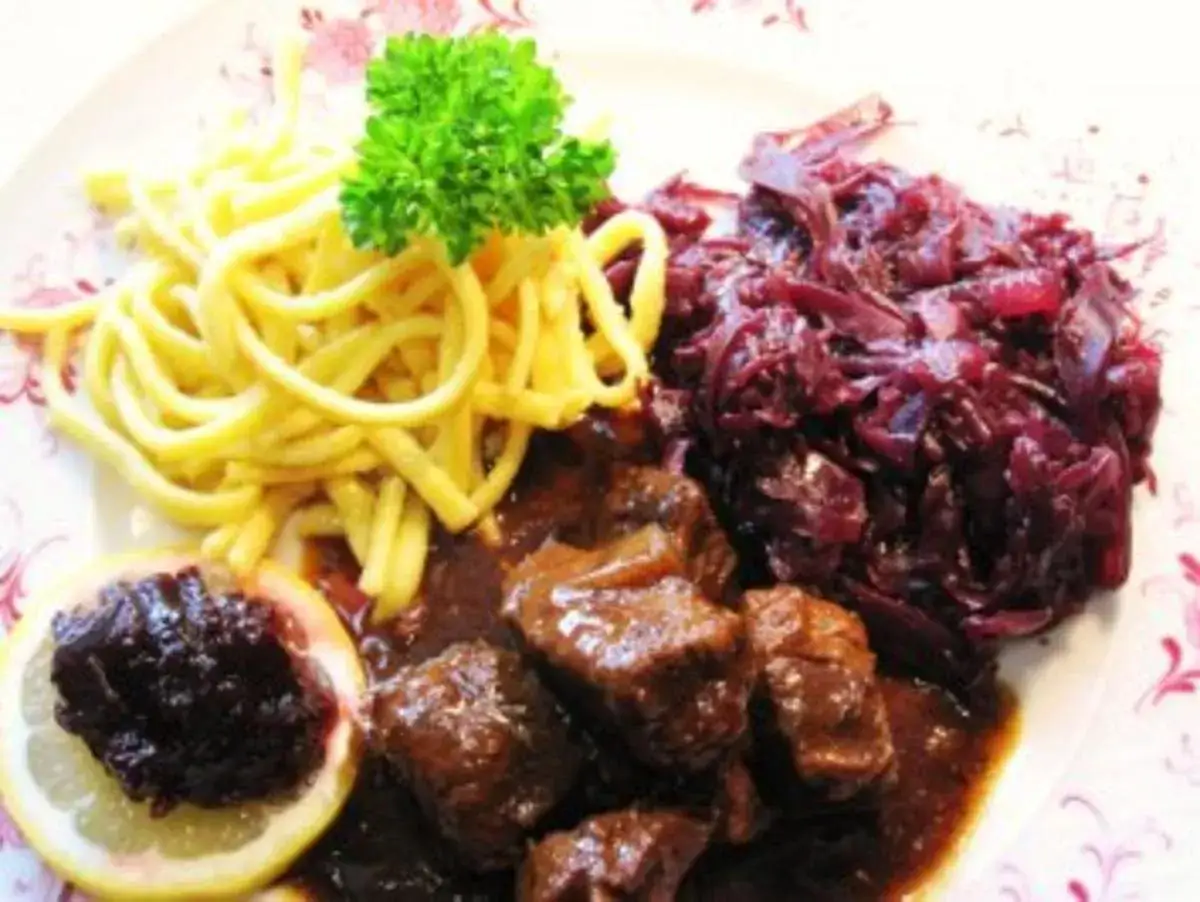 Deftiges Gulasch mit Spätzle und einem köstlichen rotkohl rezept. Garniert mit Petersilie und einer Zitronenscheibe.