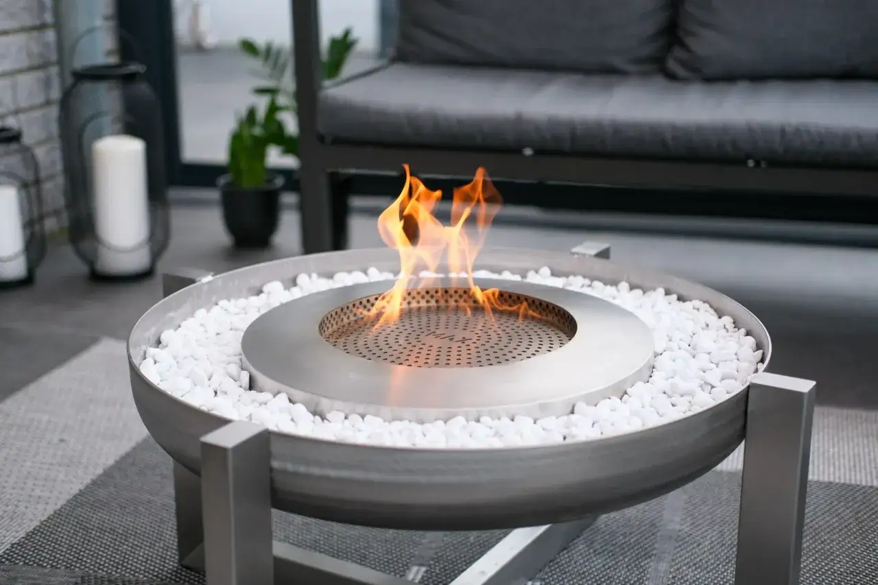 En modern eldstad utan skorsten med flammande gaseld, omgiven av vita stenar. Perfekt f&ouml;r mysiga kv&auml;llar p&aring; uteplatsen.