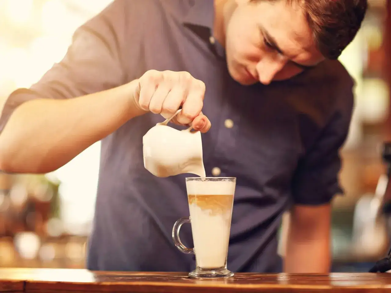 Barista gie&szlig;t Milch in ein Glas mit Kaffee. So macht man einen Latte Macchiato.