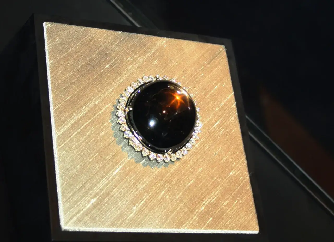 Ein glänzender schwarzer Saphir mit einem Stern-Effekt, umgeben von kleinen Diamanten. Seine tiefe Farbe symbolisiert Schutz und Weisheit.