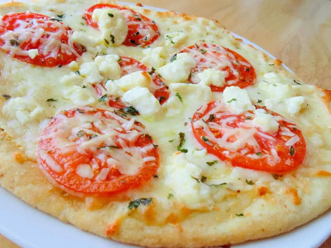 Eine Fladenbrot-Pizza mit Tomaten, zerbr&ouml;ckeltem K&auml;se und geschmolzenem K&auml;se, die an eine k&ouml;stliche quattro formaggi erinnert.