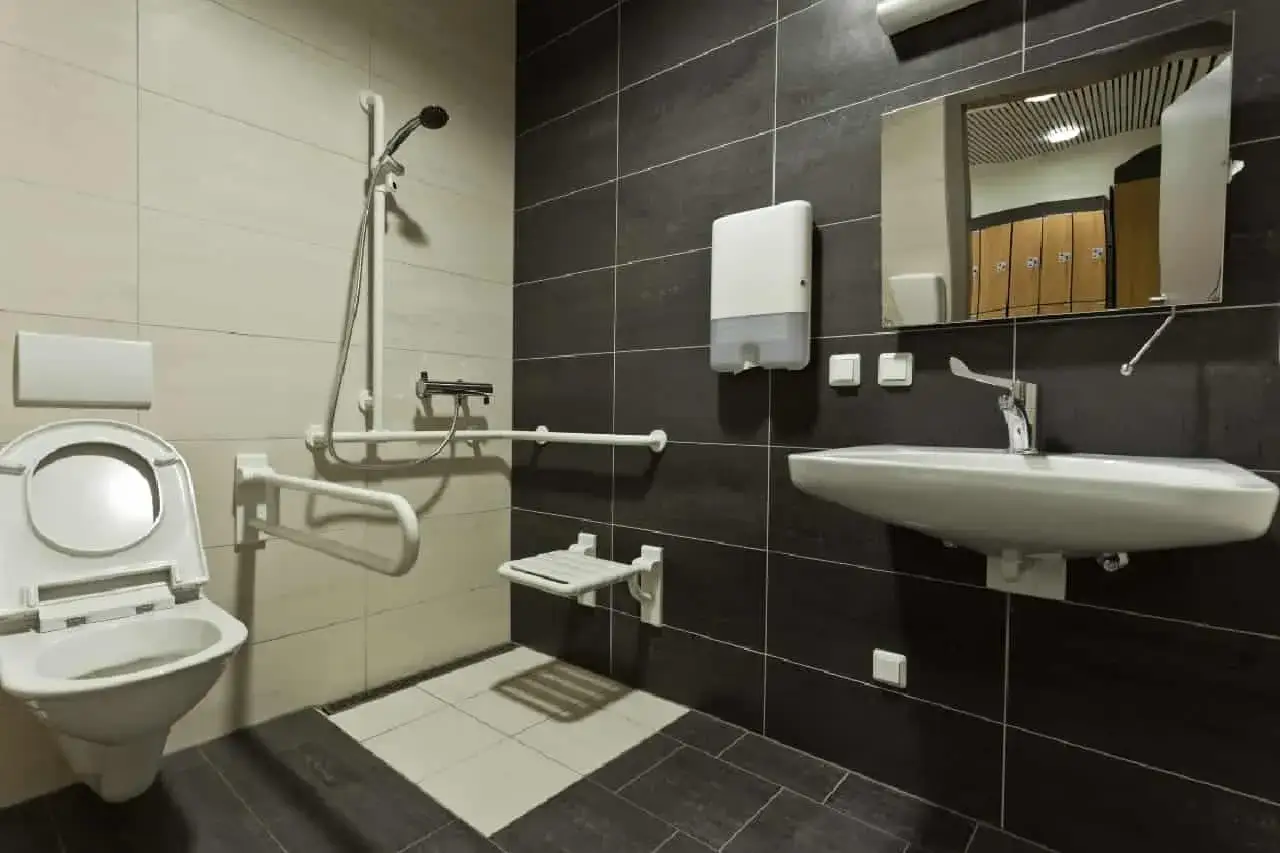 Salle de bain PMR avec cuvette, barre d'appui, si&egrave;ge de douche rabattable et lavabo. Con&ccedil;ue pour l'accessibilit&eacute;.