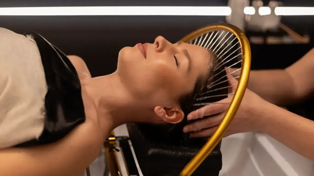 Una mujer disfruta de un tratamiento de spa para el pelo, con agua cayendo suavemente sobre su cabeza.