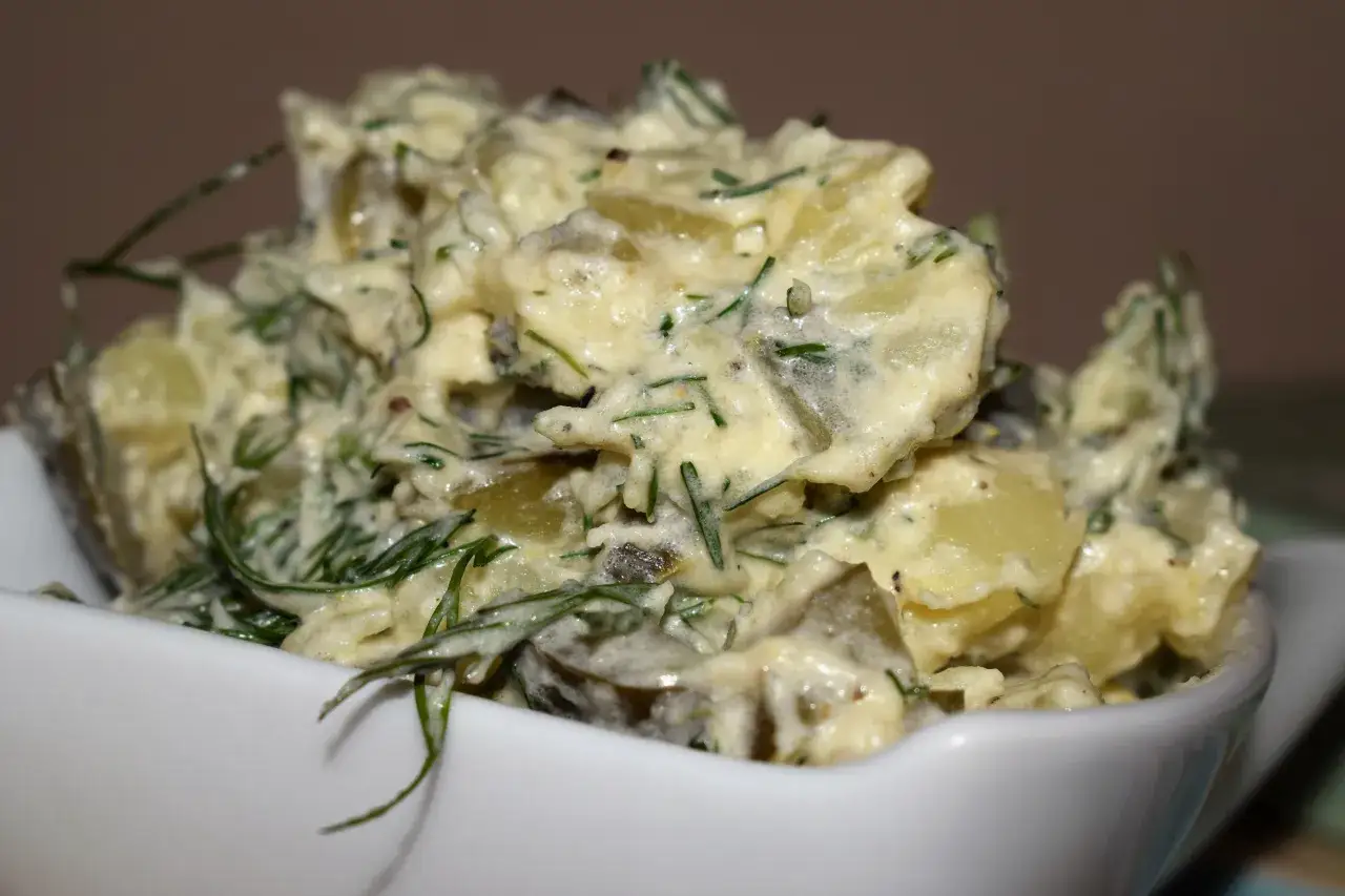 Kremowy kartofel salad z koperkiem i ogórkiem kiszonym, podany w białej miseczce.
