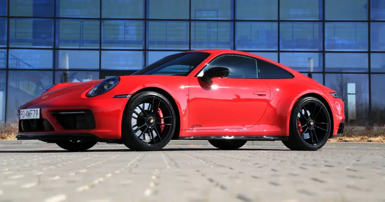 Czerwone Porsche 911 GTS, symbol niezawodności i najmniej awaryjne auta, lśni na tle nowoczesnego budynku.