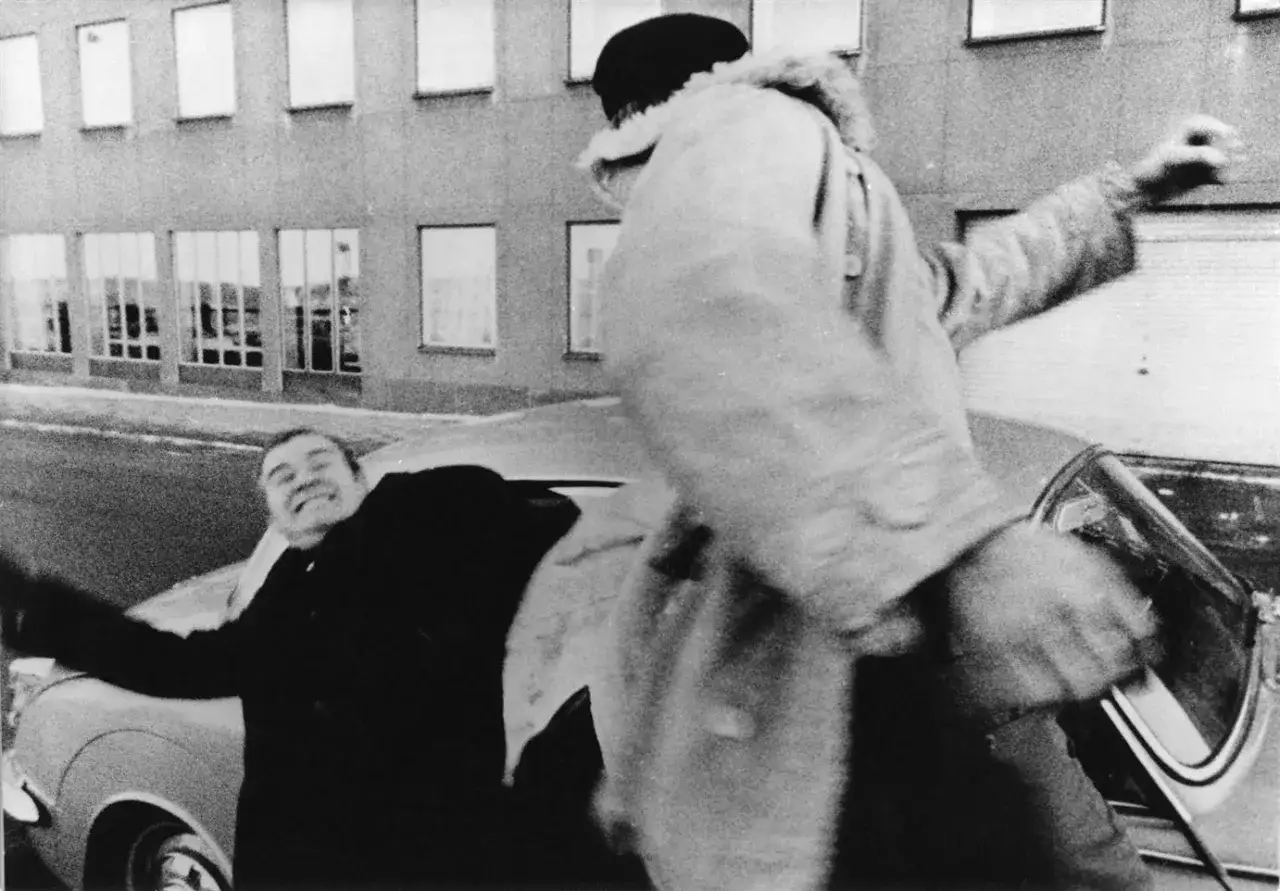 Lars Lennart Forsberg skrattar när han dras ur en bil. En person i pälsjacka drar i honom.
