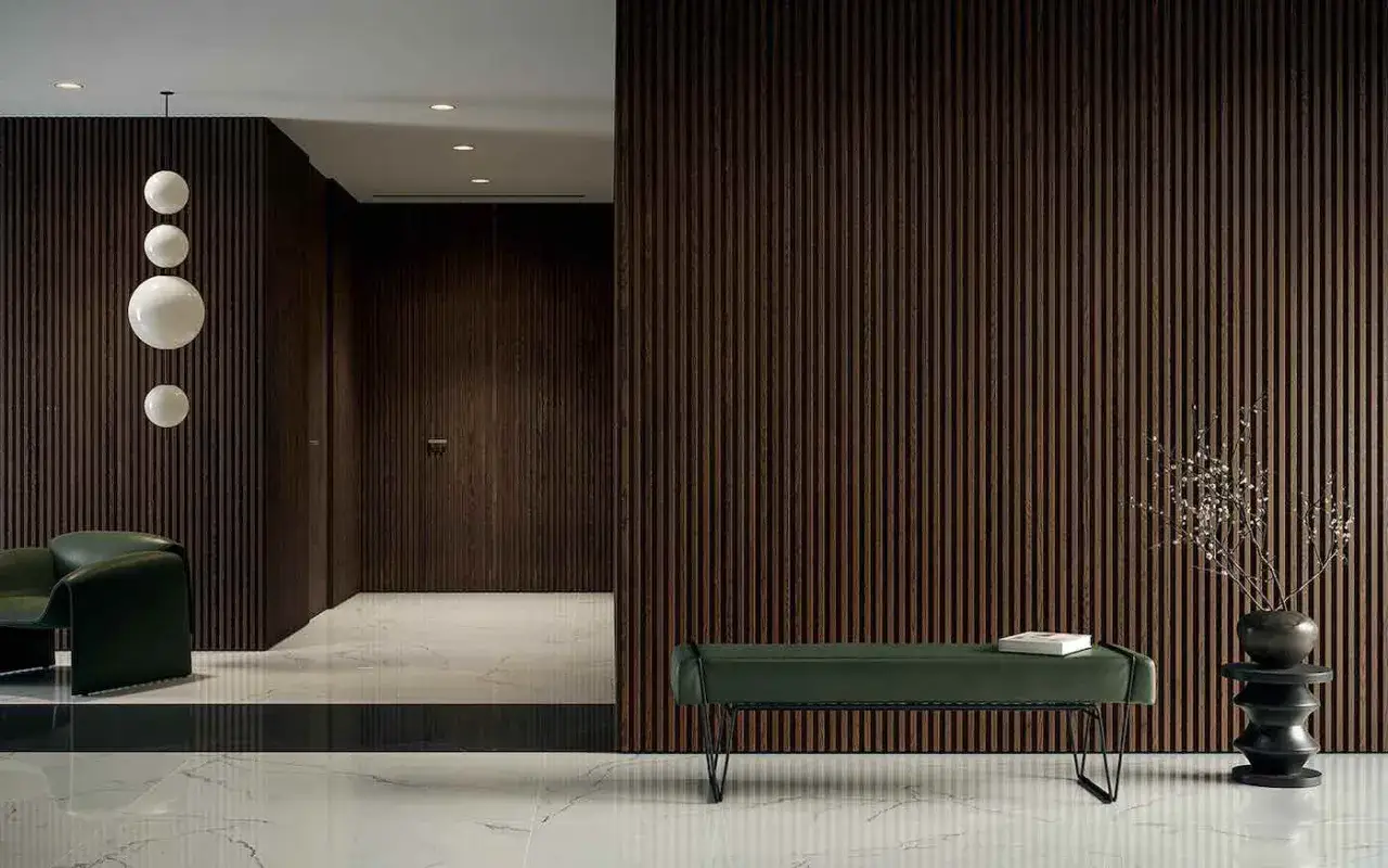 Ingresso moderno con pareti in legno scuro e soffitto alto 5 metri. Una poltrona verde e una panca completano l'arredo.
