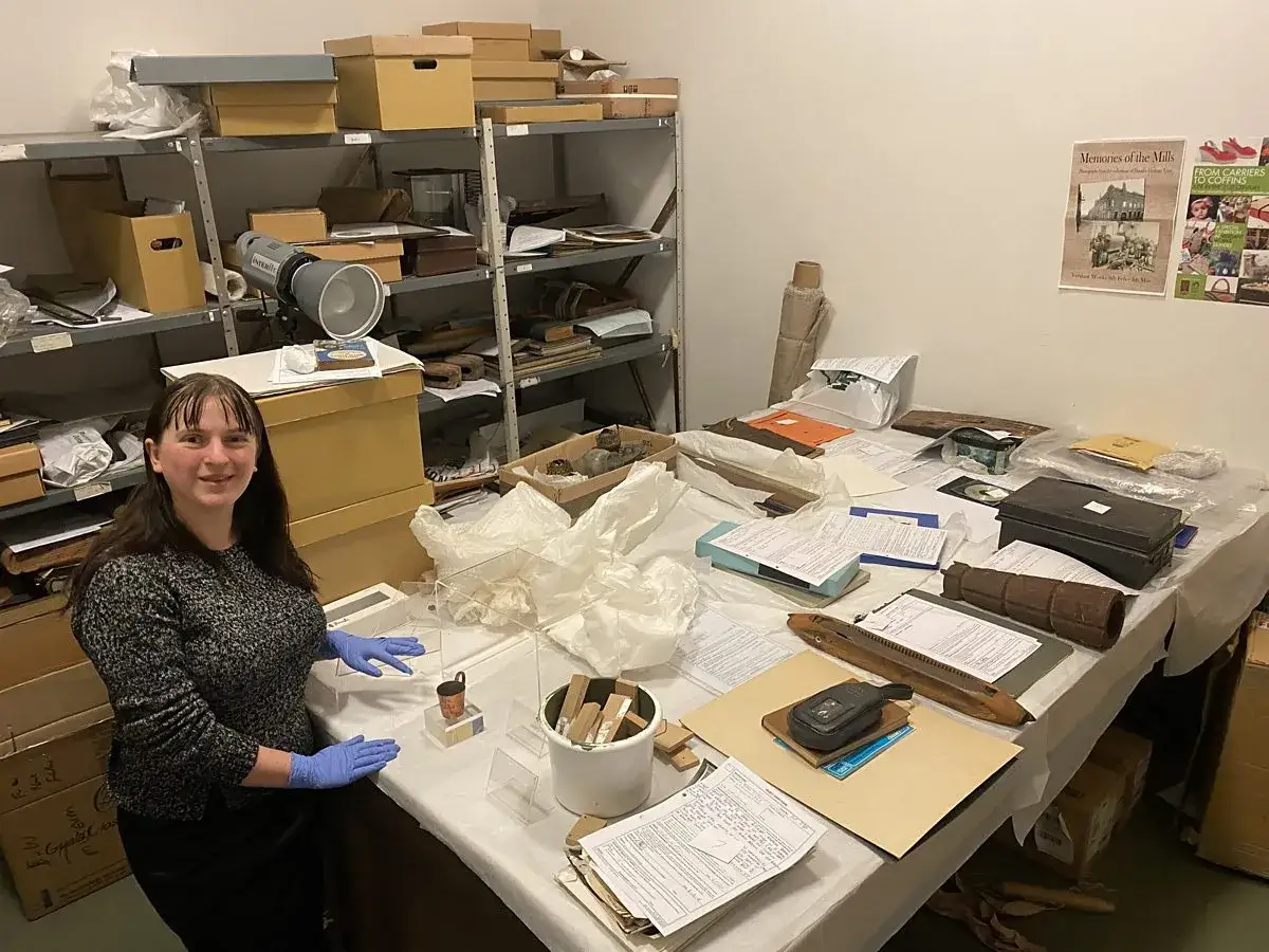 A museum worker, perhaps one of the famous art curators, prepares artifacts for display in a storage room filled with shelves of boxes and a table laden with historical items.