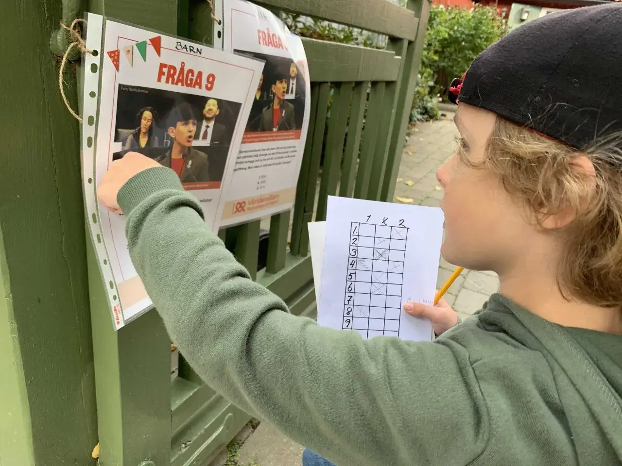 En pojke med keps l&ouml;ser en tipspromenad f&ouml;r barn. Han tittar p&aring; en fr&aring;ga och fyller i sitt svar p&aring; ett protokoll.