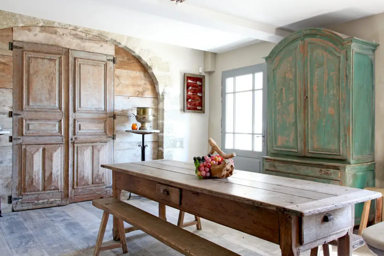 Relook et patine : une table rustique et un buffet vert vieilli, flanqués de portes anciennes en bois et d'une armoire patinée.