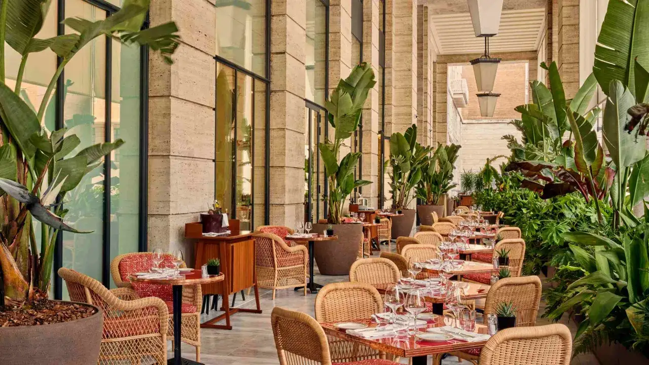 Terrazza lussureggiante con tavoli apparecchiati al Bulgari Hotel Roma, circondata da piante tropicali e arredi eleganti.