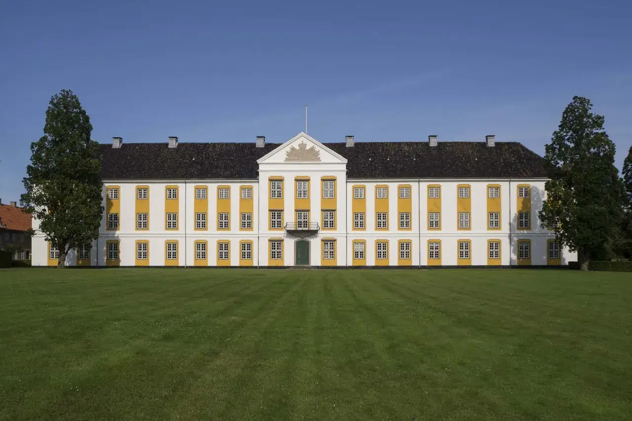 Elegancki pałac w stylu klasycyzm architektura, z ż&oacute;łtymi ramami okien i frontonem z herbem, otoczony zielonym trawnikiem.