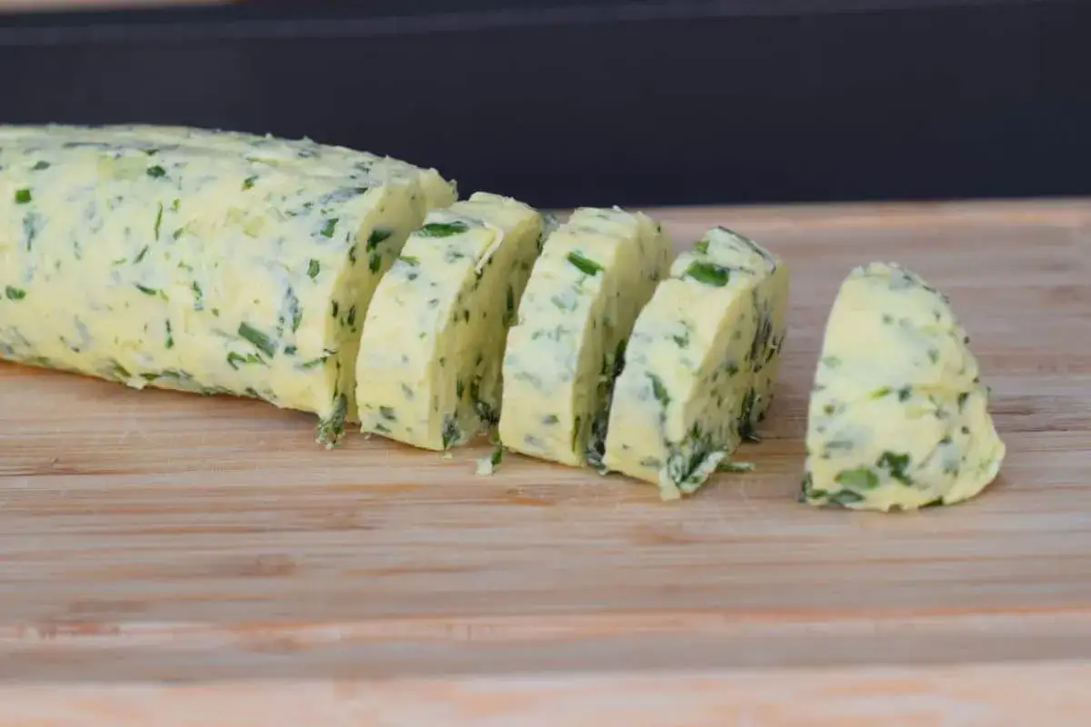 Un rouleau de beurre ma&icirc;tre d'h&ocirc;tel, coup&eacute; en tranches, parsem&eacute; d'herbes fra&icirc;ches, sur une planche en bois.