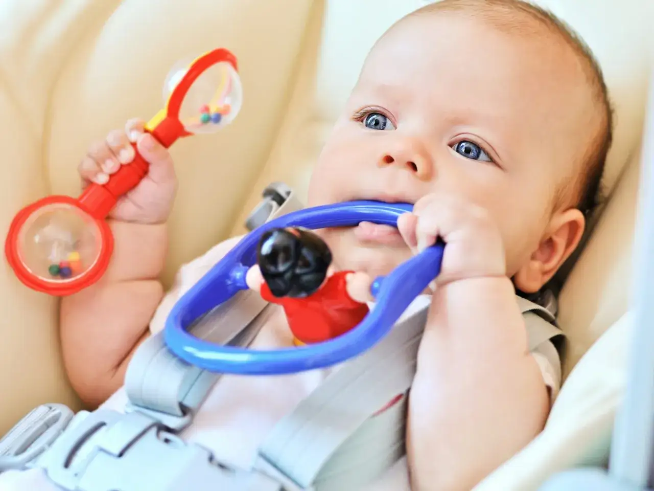 Un neonato con occhi azzurri esplora un sonaglio rosso e un gioco blu, scoprendo come stimolare il neonato ad afferrare oggetti.