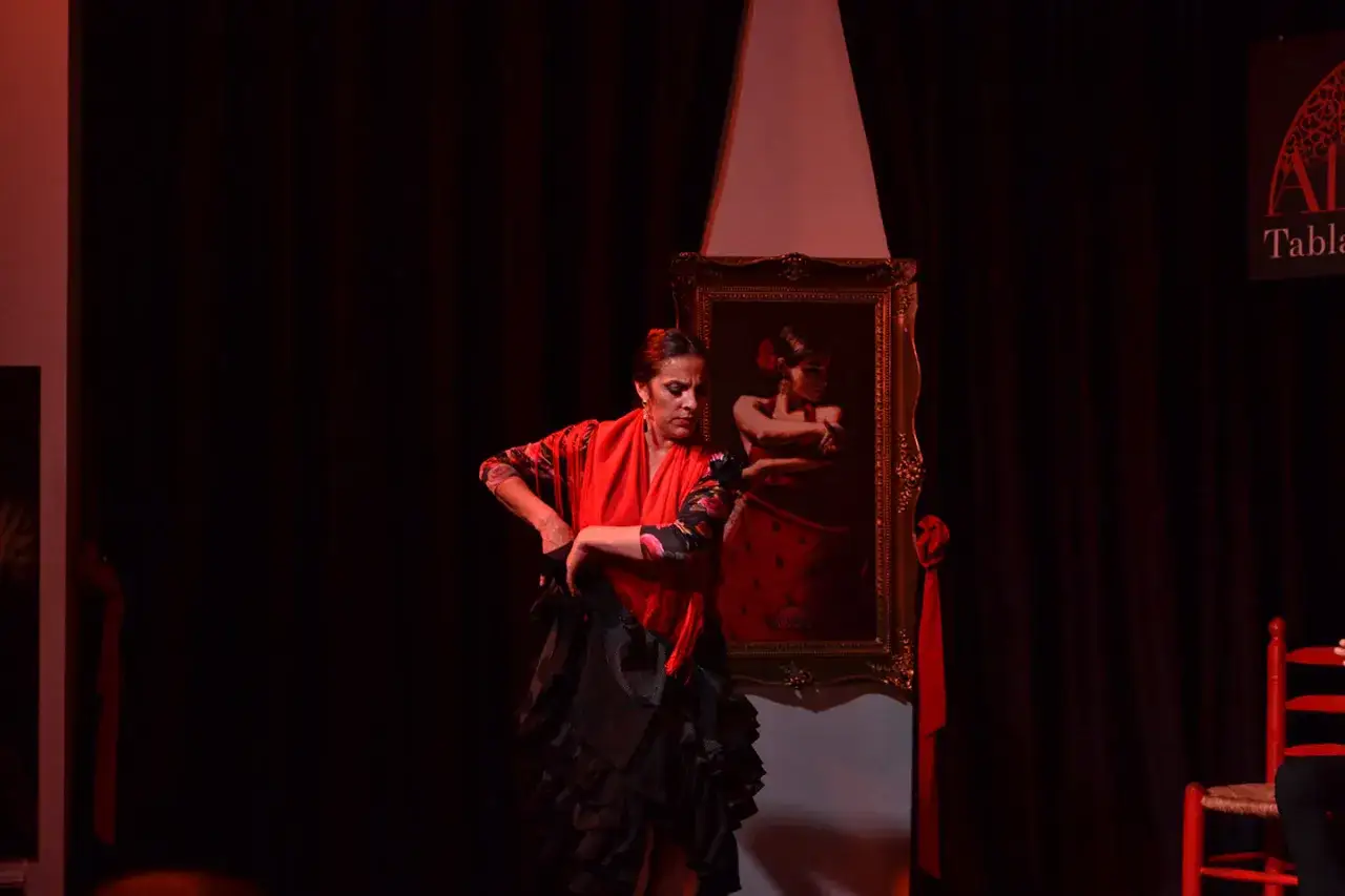 Bailarina de flamenco en el escenario, con un cuadro de otra artista de la alborea de fondo.