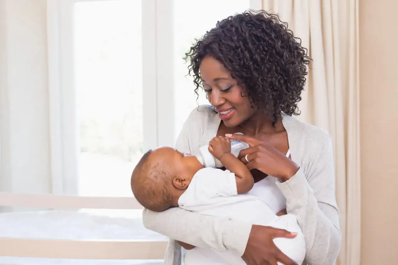 Uśmiechnięta mama karmi noworodka butelką, pokazując, jak karmić noworodka butelką.