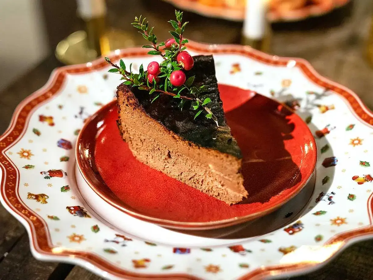 En bit krämig choklad cheesecake med en glansig yta och dekorerad med lingonris. Serverad på en vacker jultallrik.