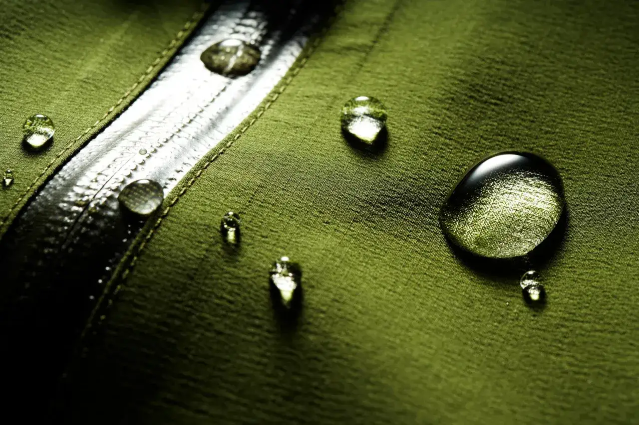 Gocce d'acqua su tessuto verde, dimostrando il **water repellent significato** di protezione.