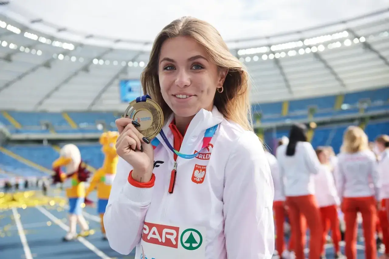 Klaudia Adamek z dumą prezentuje złoty medal na stadionie.
