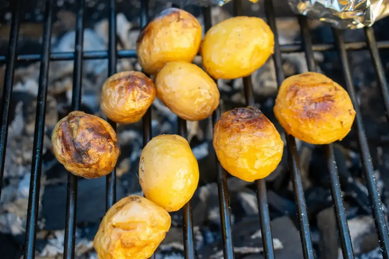 Kleine, goldbraune Kartoffeln garen auf dem Grill. Einige sind leicht angekohlt, andere noch hellgelb. Ein köstlicher Anblick!