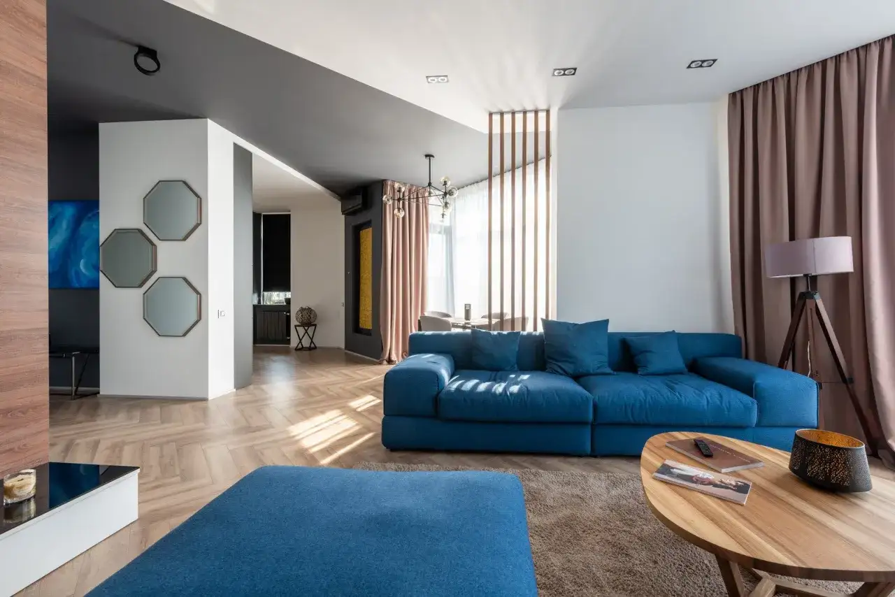 Nowoczesny salon z niebieską kanapą, drewnianą podłogą i geometrycznymi lustrami. Ten styl wnętrz jest pełen elegancji.