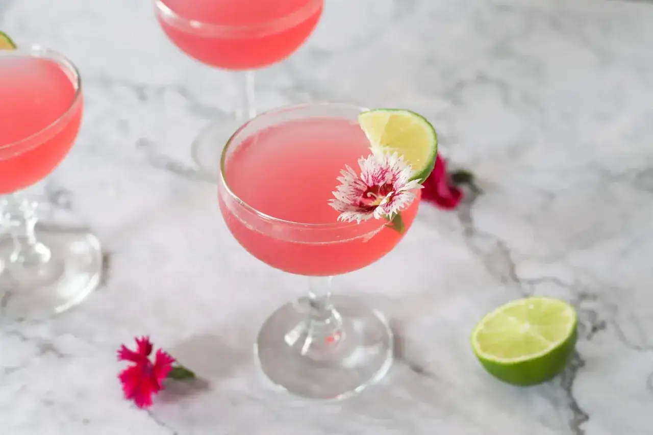 Ein Cosmopolitan Cocktail, garniert mit Limette und Bl&uuml;te, auf Marmoruntergrund.
