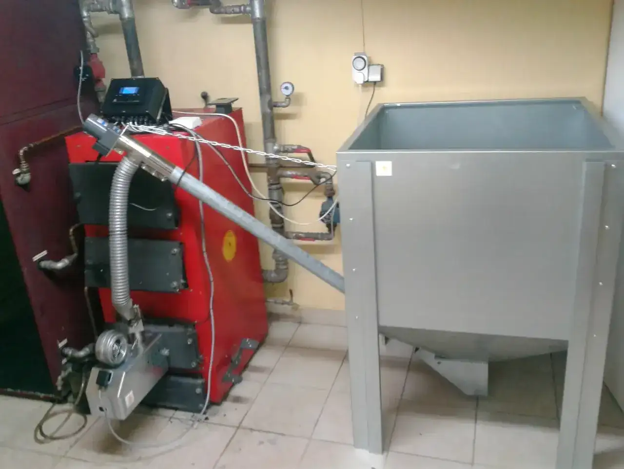 Instalacja do ogrzewania: czerwony piec na ekogroszek z podajnikiem i zasobnikiem na pellet.