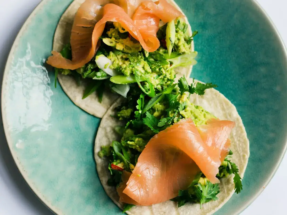 Deux tortillas garnies d'un délicieux wrap saumon avocat, d'avocat écrasé, de coriandre fraîche et d'oignons verts sur une assiette turquoise.