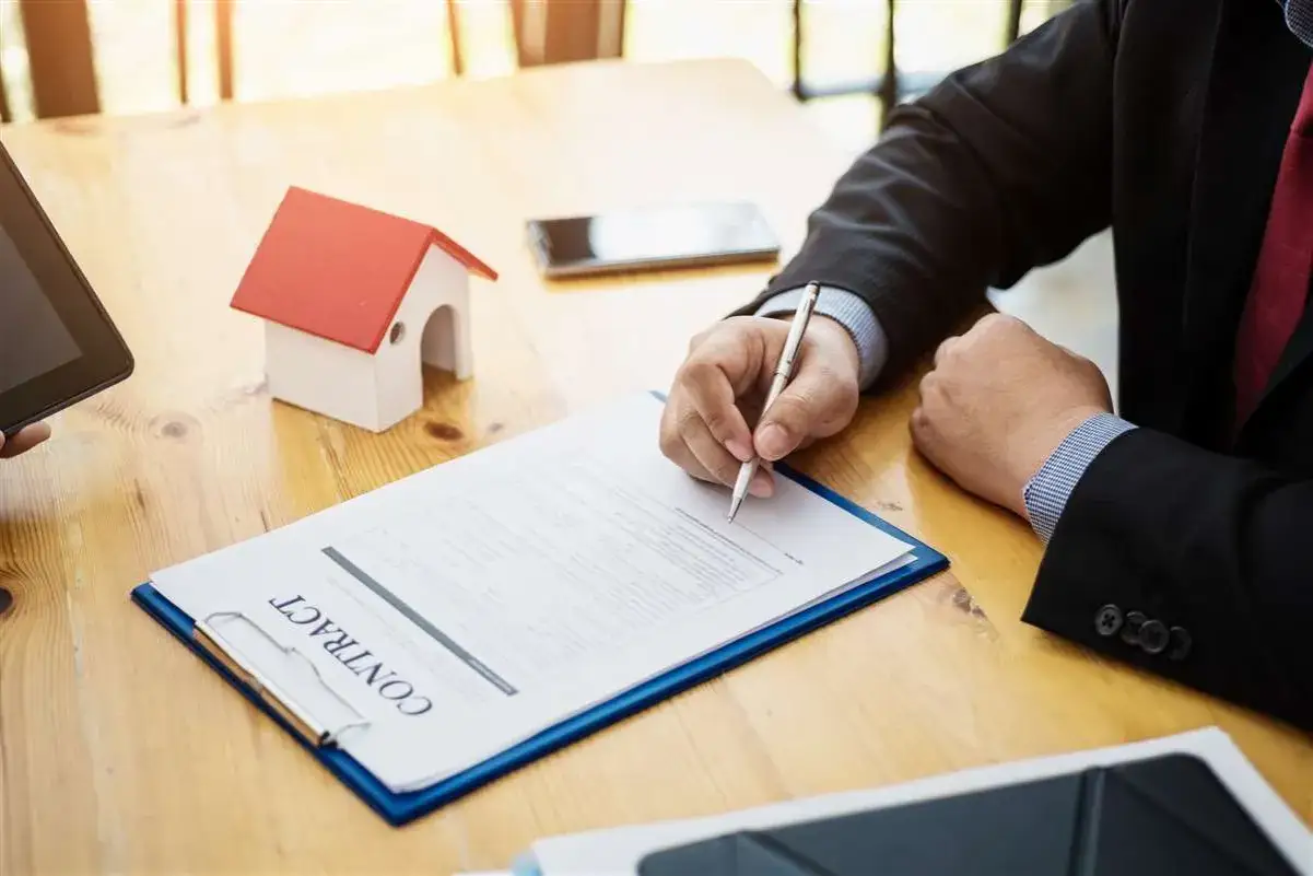 Firma su contratto immobiliare, con una miniatura di casa e un tablet. Si discute la garanzia per evizione significato.