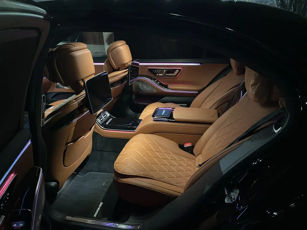 Wnętrze luksusowego Mercedesa S400d z brązową skórzaną tapicerką, ambientowym oświetleniem i ekranami multimedialnymi.