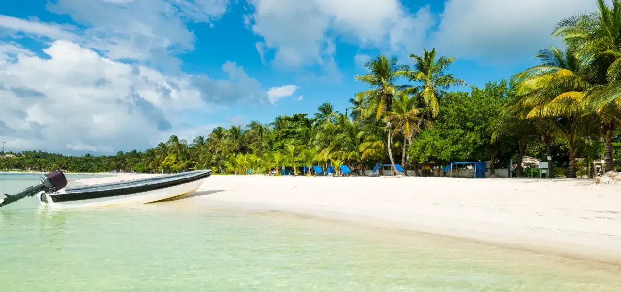 Playa caribe&ntilde;a con palmeras, arena blanca y un bote. Un lugar ideal para descubrir qu&eacute; ver en Colombia.
