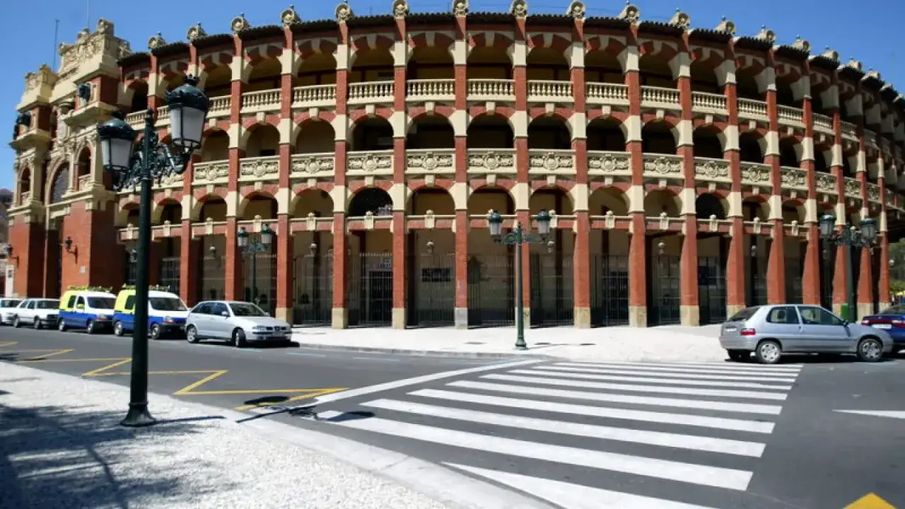 La plaza de la Misericordia en Zaragoza, con su arquitectura de ladrillo y arcos, se alza majestuosa. Coches aparcados y un paso de peatones completan la escena.