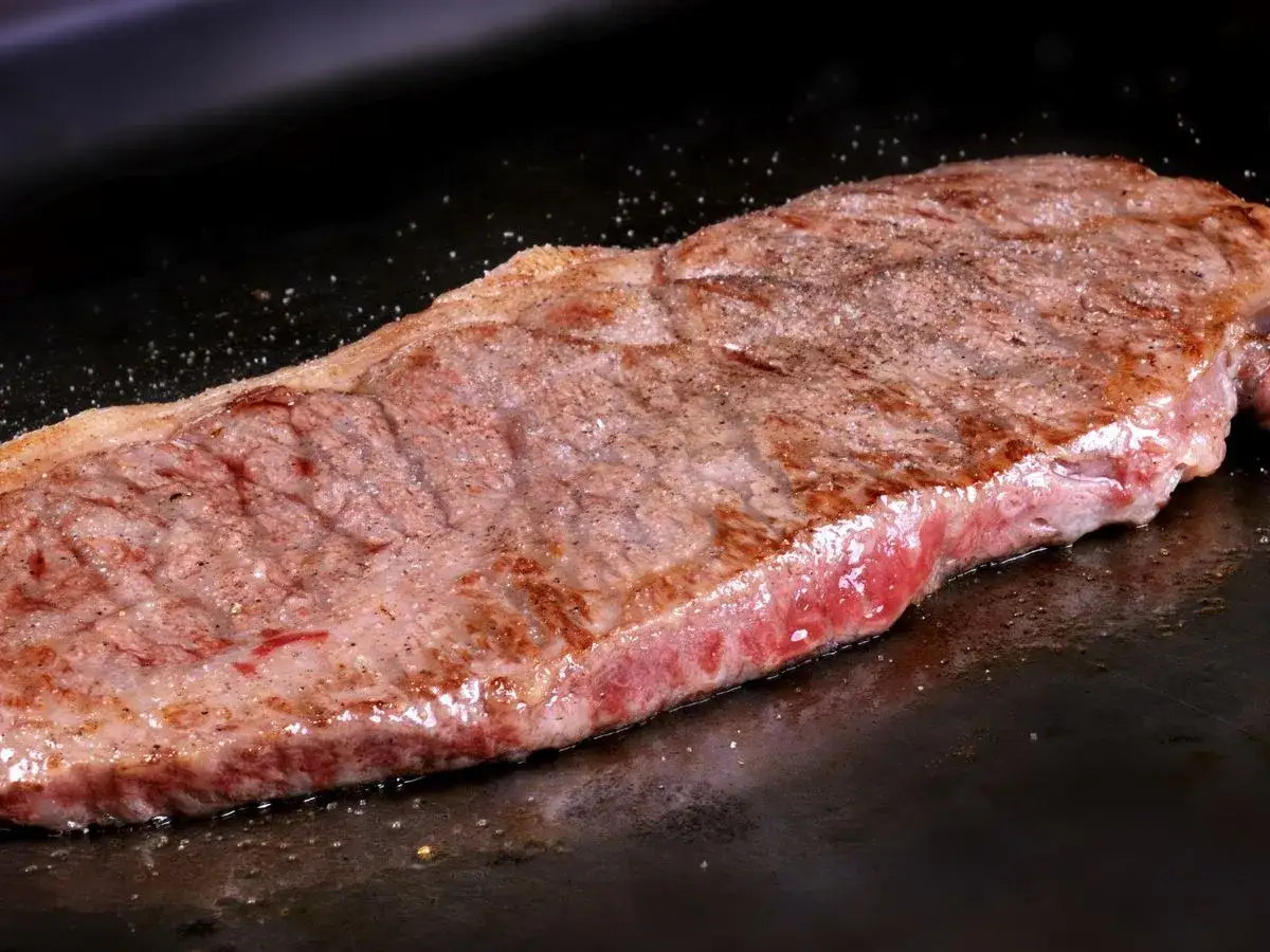 Un jugoso filete de ternera se cocina a la perfección en una plancha caliente, con sal y pimienta esparcidas.