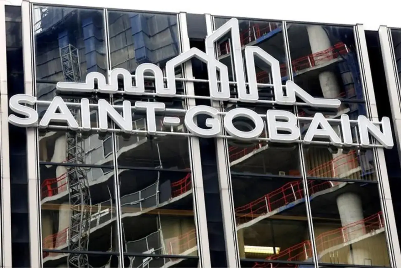 Logo Saint-Gobain na szklanej fasadzie budynku, odbijającej konstrukcję schodów i dźwig budowlany. Akcje Saint-Gobain rosną.