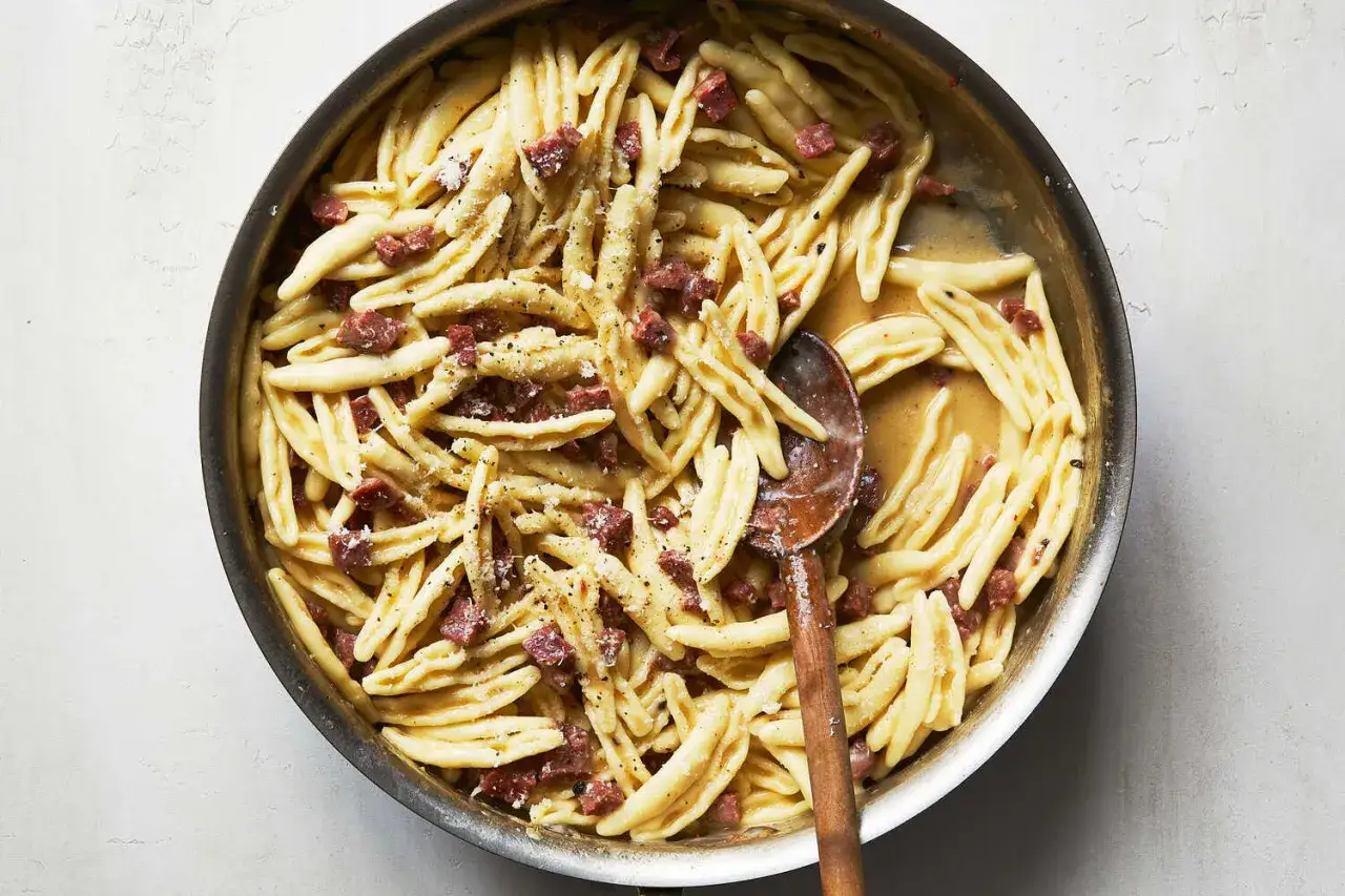 En panna med krämig pasta med små bitar av salami, toppad med riven ost och svartpeppar. Enkel och god pasta med salami.