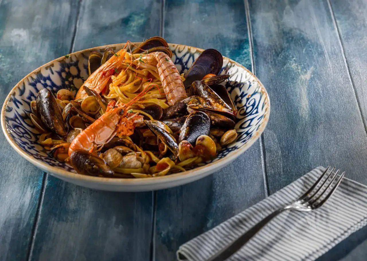 Piatto di pasta ai frutti di mare, con gamberi e scampi, servito in una ciotola decorata. Un assaggio del ristorante Amerigo Rimini.