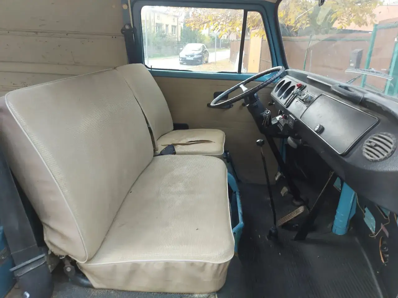 Wnętrze klasycznego VW T2 z jasnymi siedzeniami i widokiem na ulicę przez okno.