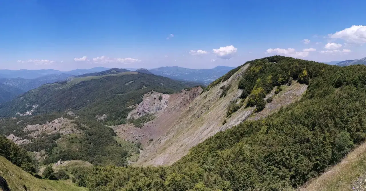 Panoramica mozzafiato dal passo Zovallo, con valli boscose e pendii rocciosi sotto un cielo azzurro.
