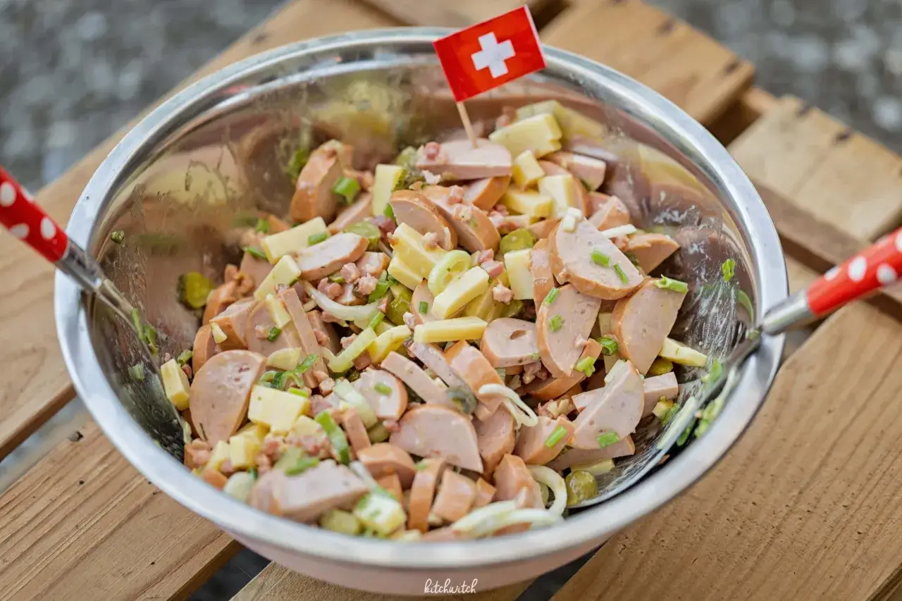 Schmackhafter Schweizer Wurstsalat mit K&auml;sew&uuml;rfeln, Gurken und Schnittlauch, garniert mit einer Schweizer Flagge.