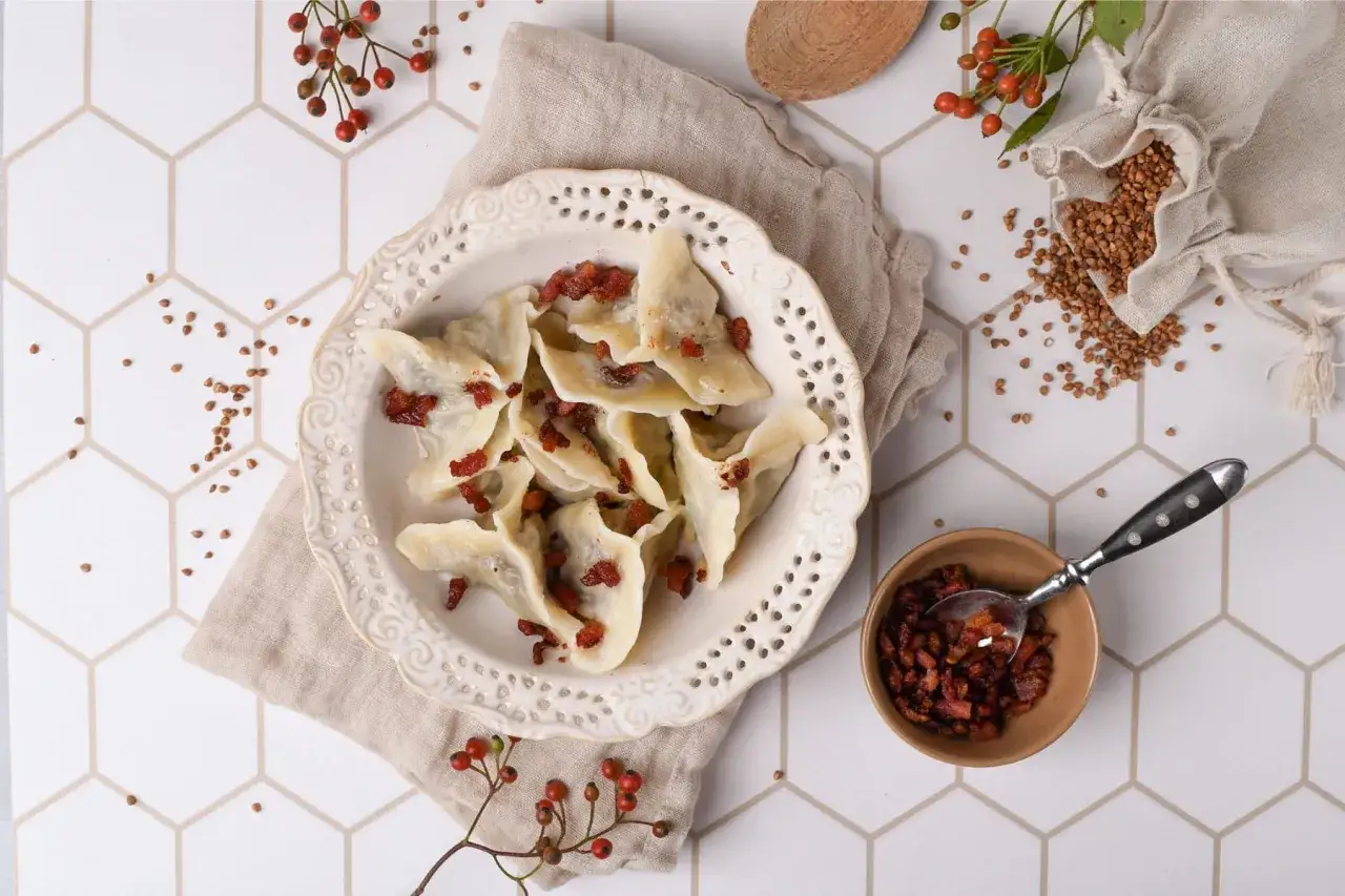 Talerz pełen pierogów z boczkiem, obok miseczka z dodatkami i woreczek z kaszą gryczaną. Zastanawiasz się, ile wychodzi pierogów z 1kg mąki?
