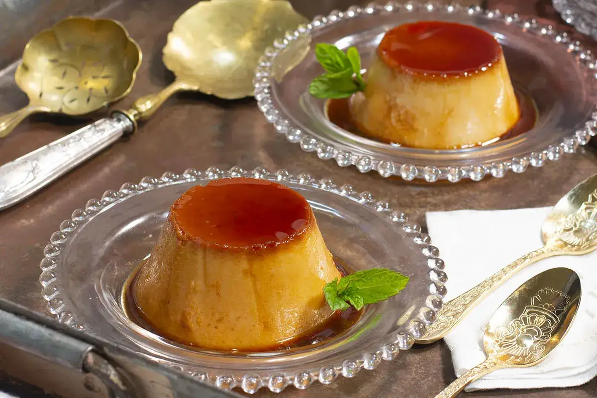 Dos deliciosos flanes de huevo caseros, ba&ntilde;ados en caramelo y decorados con menta, servidos en platos de cristal.