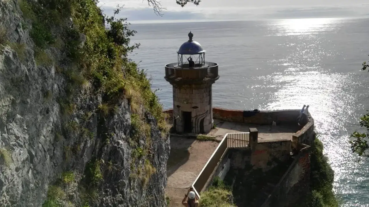 Un faro solitario se alza sobre un acantilado rocoso en Cantabria, vigilando el mar brillante.