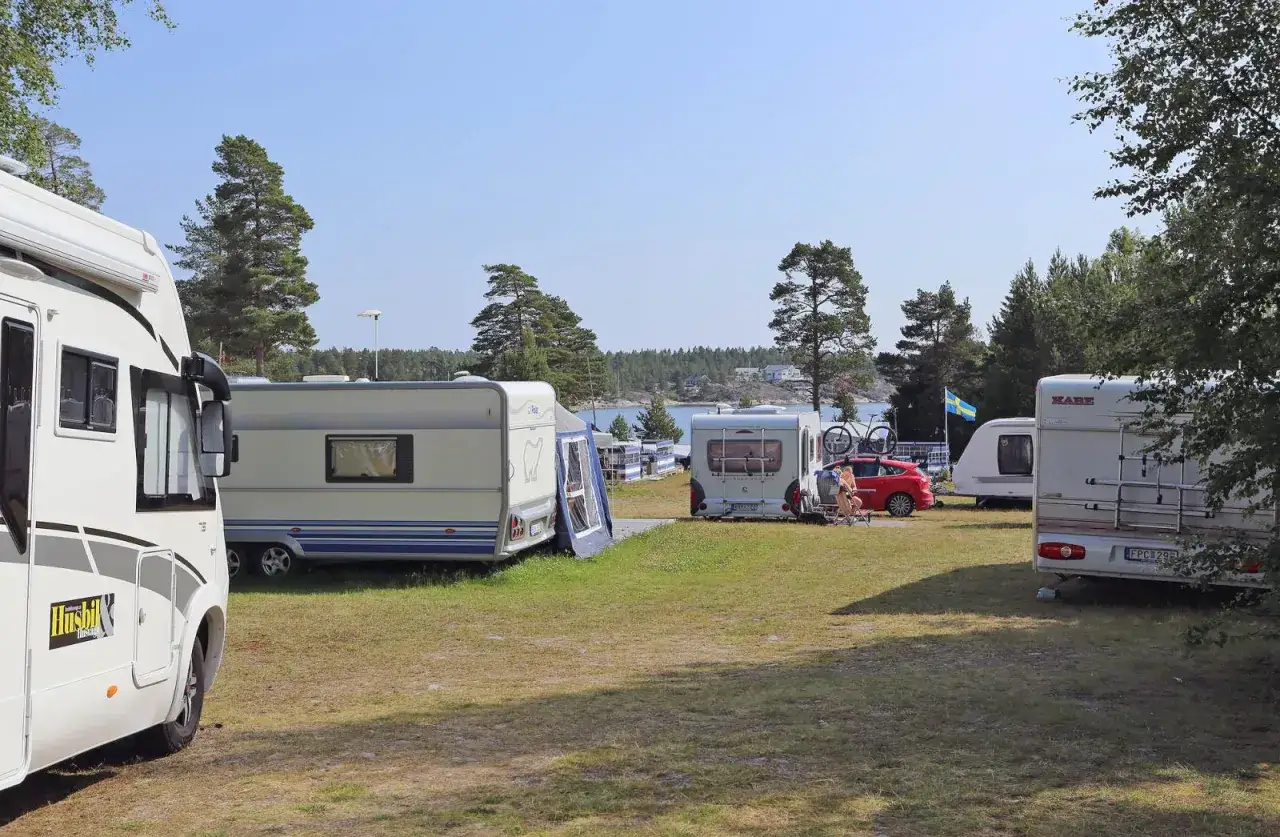 Solig dag p&aring; camping norrlandskusten med husbilar och husvagnar uppst&auml;llda vid vattnet.