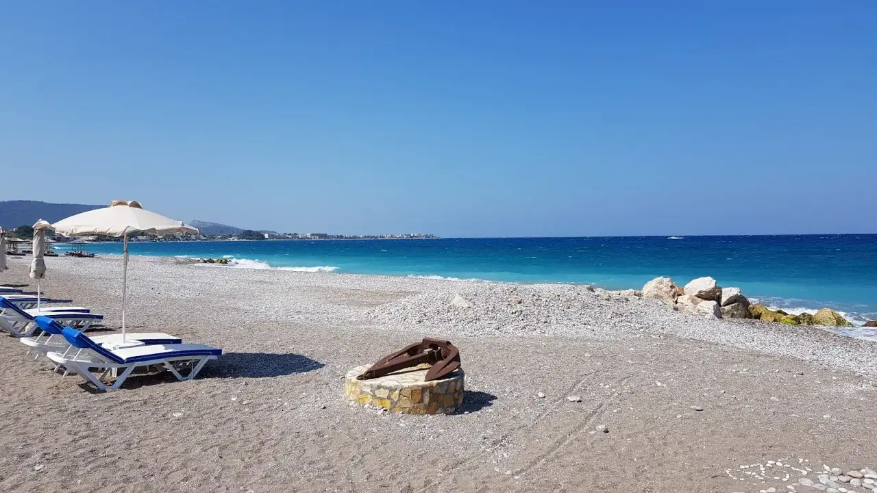 Słoneczna plaża w Ixia, Rodos, z leżakami, parasolem i starym kotwicą.