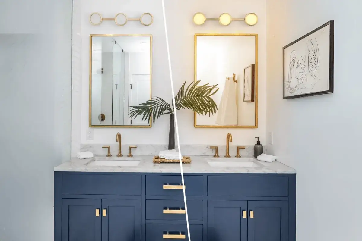 A modern bathroom vanity with two sinks, a navy blue cabinet, and 2 or 3 lights over each gold-framed mirror.