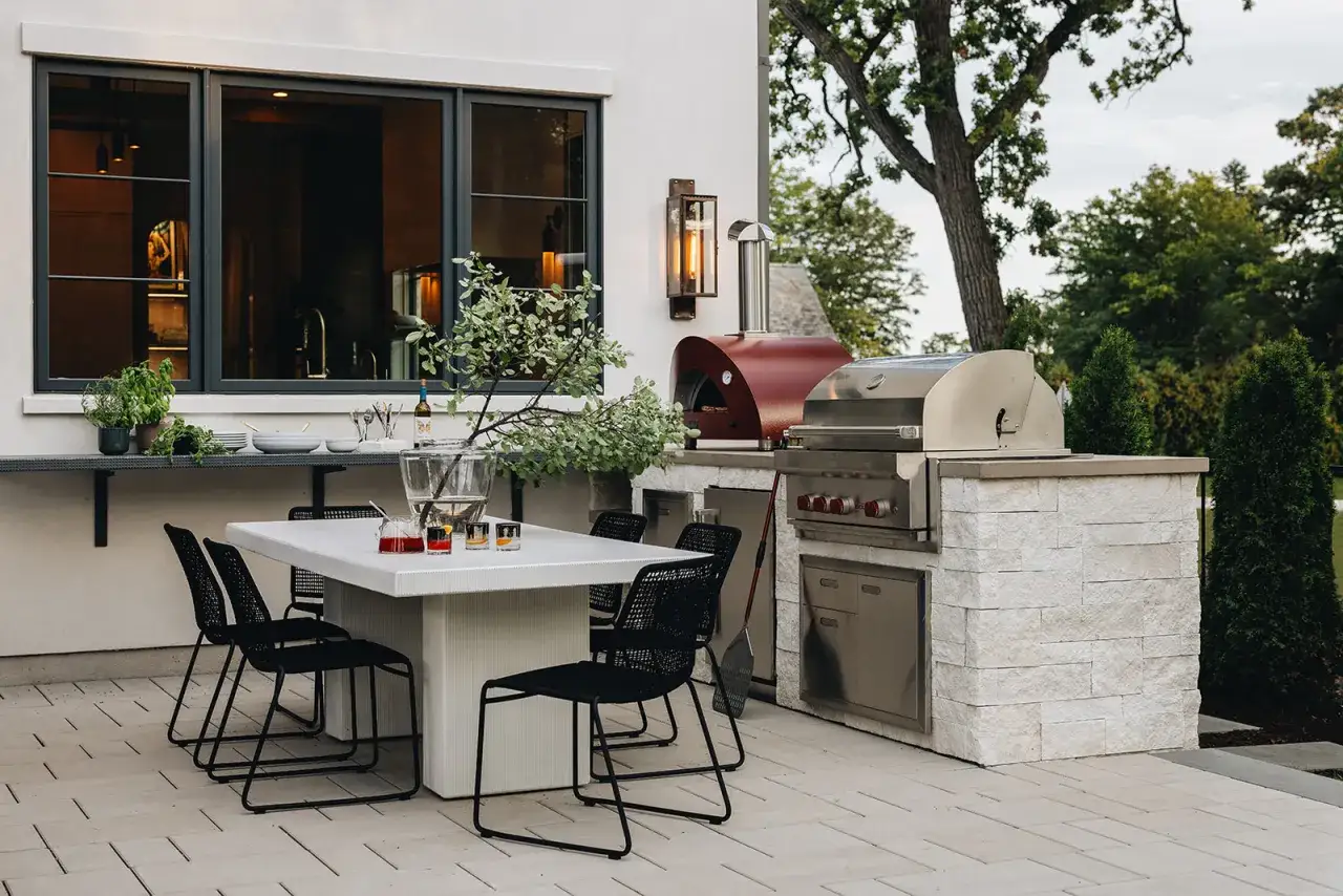 Moderna zona barbacoa exterior con horno de pizza y parrilla. Mesa y sillas listas para disfrutar de una comida al aire libre.