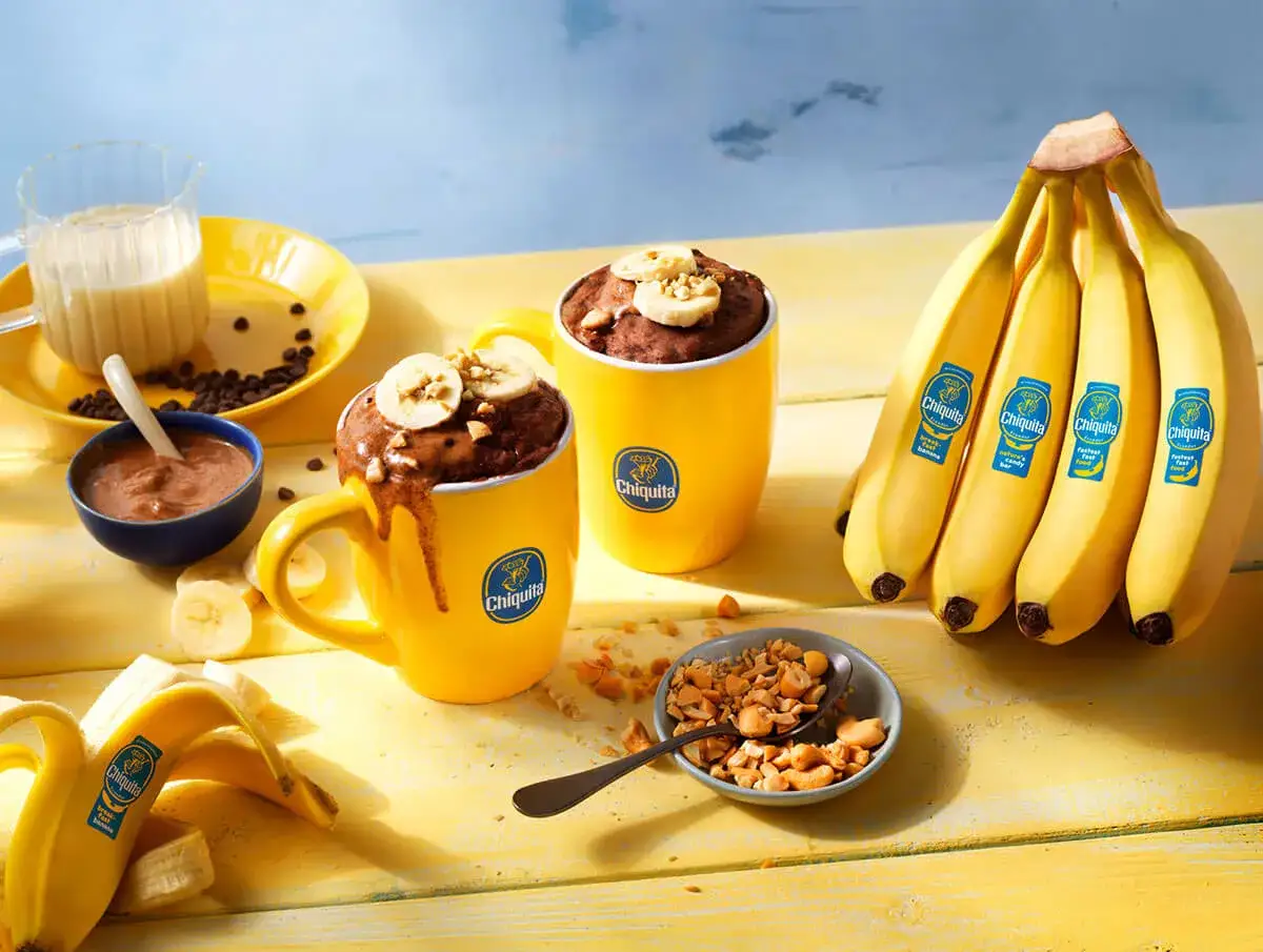 Deux mug cakes banane au chocolat, garnis de rondelles de banane et de noix, prêts à être dégustés.